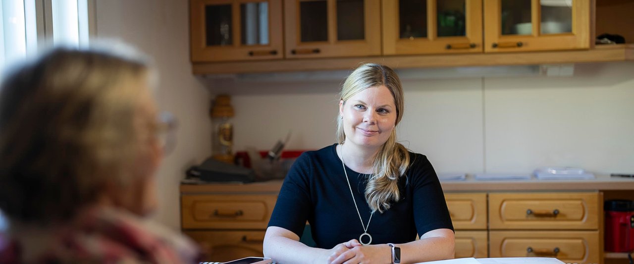 Kiinteistönvälittäjä Carita Nikander hymyilee asiakkaalle keittiön pöydän ääressä asiakastapaamisessa.